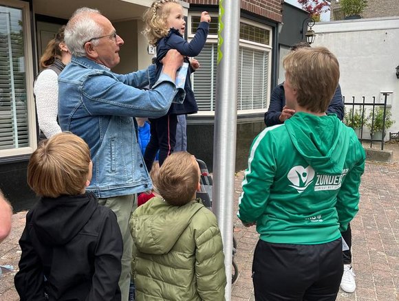 Man tilt kindje op voor oefening van de fitroute.